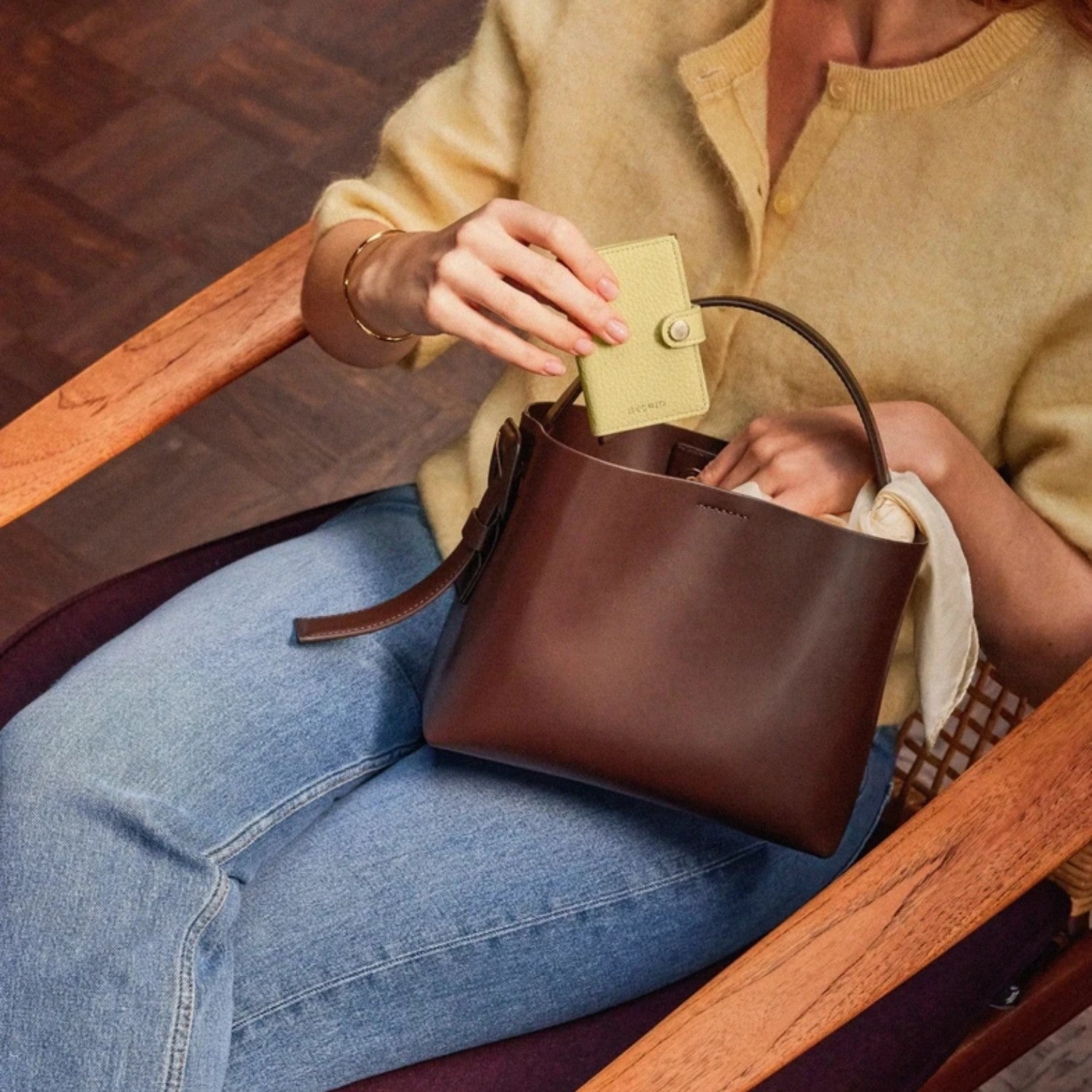 Lieblingstasche Secrid Miniwallet Pebble in light yellow leather being placed into a dark brown leather handbag