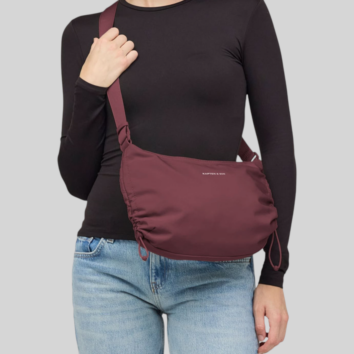 A woman wearing a Lieblingstasche Skara Small burgundy crossbody bag with adjustable side drawstrings.