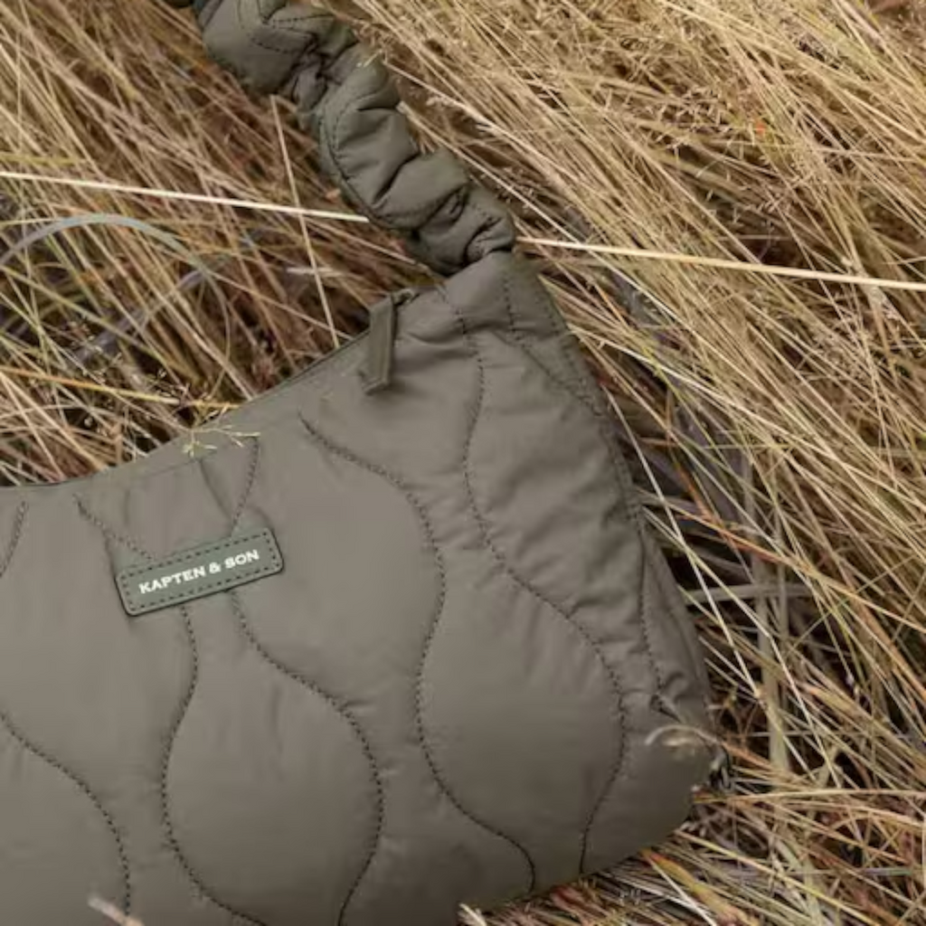 Lieblingstasche Skara Small Quilted bag in olive green with a ruched handle, resting in dry grass.