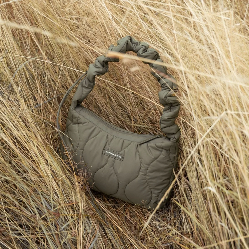 Lieblingstasche Skara Small quilted olive green handbag with a ruched handle, set in tall dry grass.