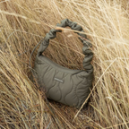 Lieblingstasche Skara Small quilted olive green handbag with a ruched handle, set in tall dry grass.