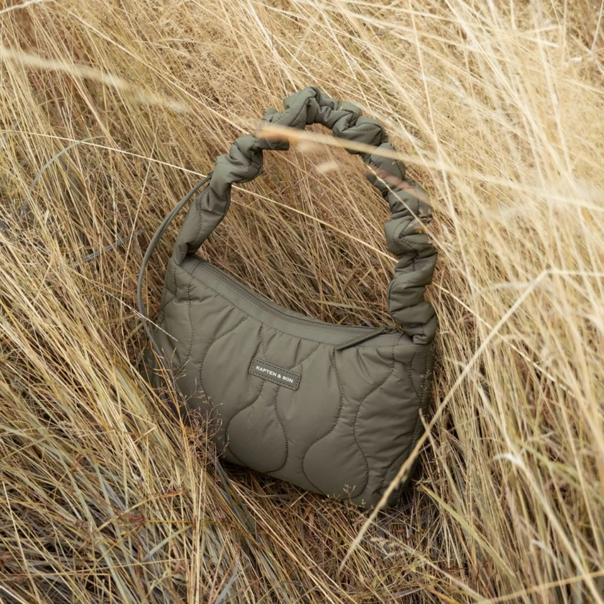 Lieblingstasche Skara Small quilted olive green handbag with a ruched handle, set in tall dry grass.