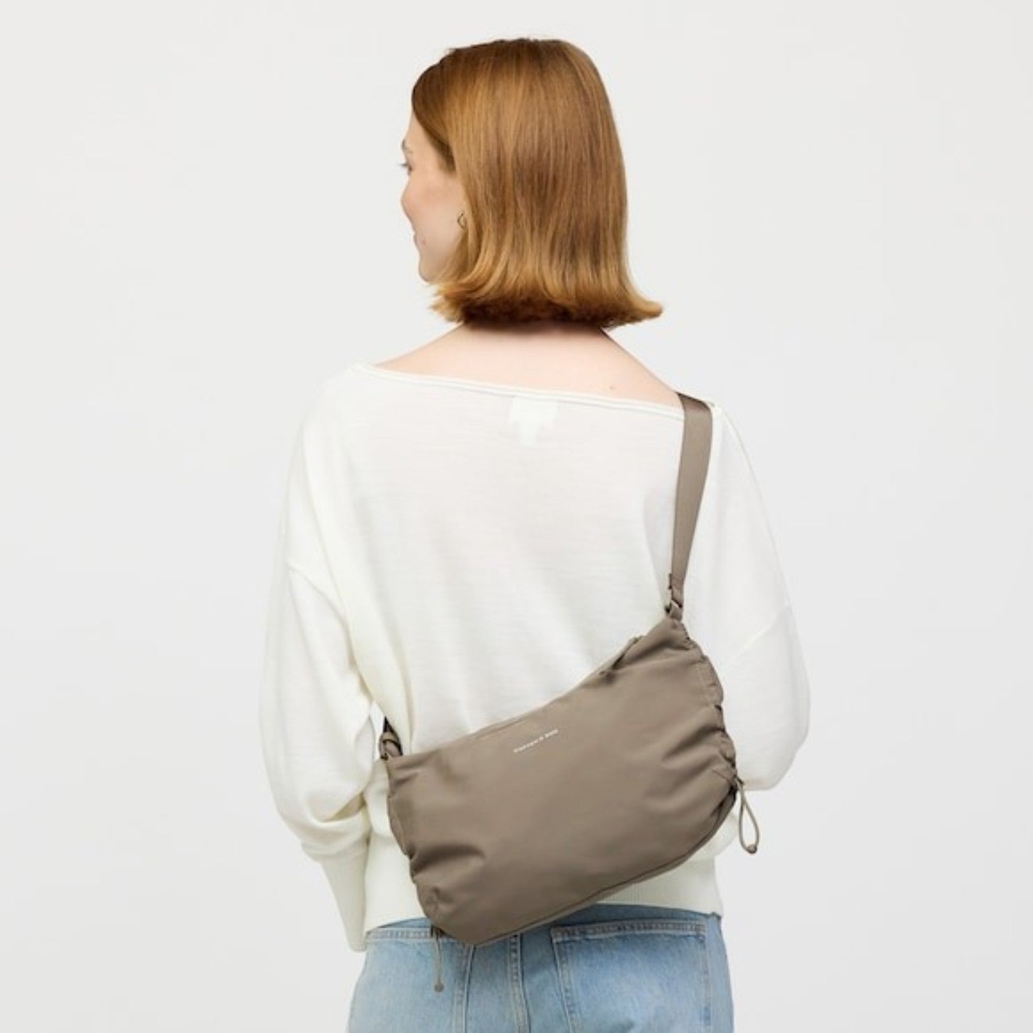 Lieblingstasche Skara Small taupe crossbody bag worn by a woman in a white sweater, showing a ruched side detail.