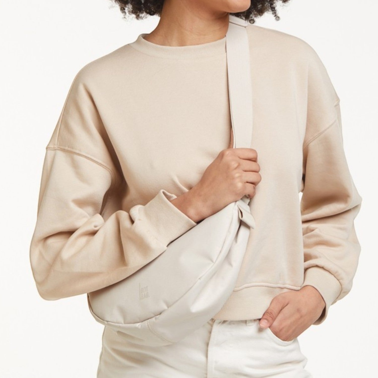 Lieblingstasche small moon bag in light beige, worn crossbody by a woman with curly hair.