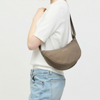 Lieblingstasche Essential Moon Bag in taupe worn over the shoulder by a woman in a white top and blue jeans