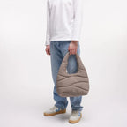 Lieblingstasche wavy puffer shoulder bag in taupe held by a smiling man wearing a white long-sleeve shirt and jeans.