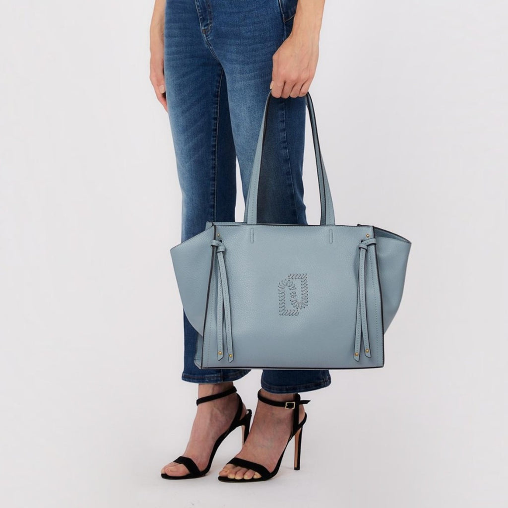 Lieblingstasche Tote L in light blue leather with side tie details held by a woman in jeans and black heels