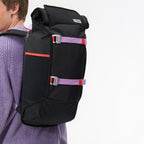 Lieblingstasche Trip Pack black roll-top backpack with purple and orange straps worn by a man in a lilac sweater