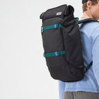 Lieblingstasche Trip Pack black backpack with teal straps worn by a man in a light blue long-sleeve shirt