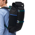 A man wearing a black Lieblingstasche Trip Pack backpack with blue and green strap accents against a white background