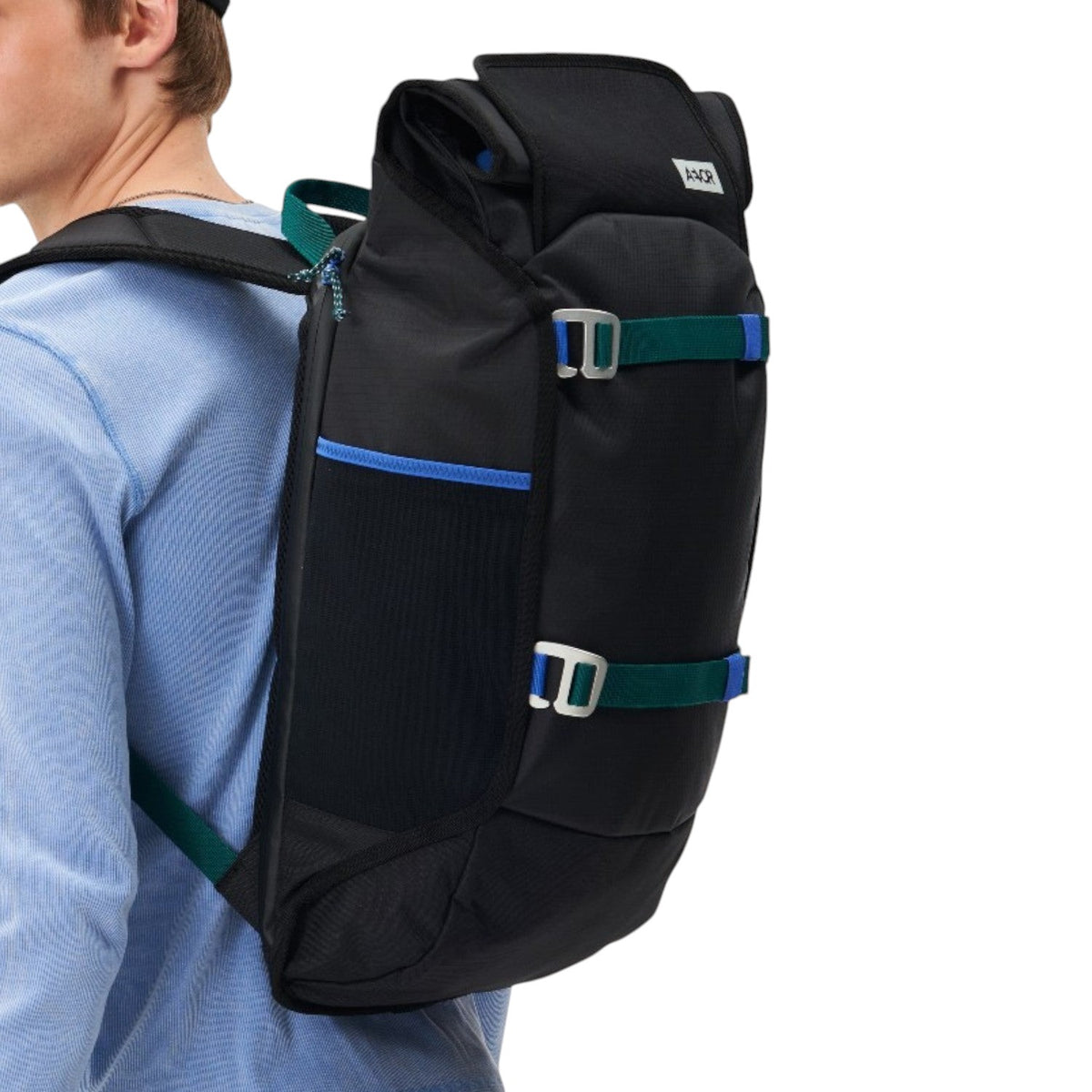 A man wearing a black Lieblingstasche Trip Pack backpack with blue and green strap accents against a white background